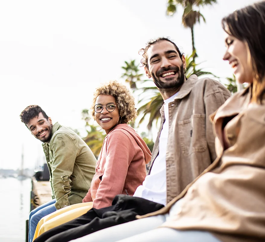 a group of smiling people sit outside by a body of water