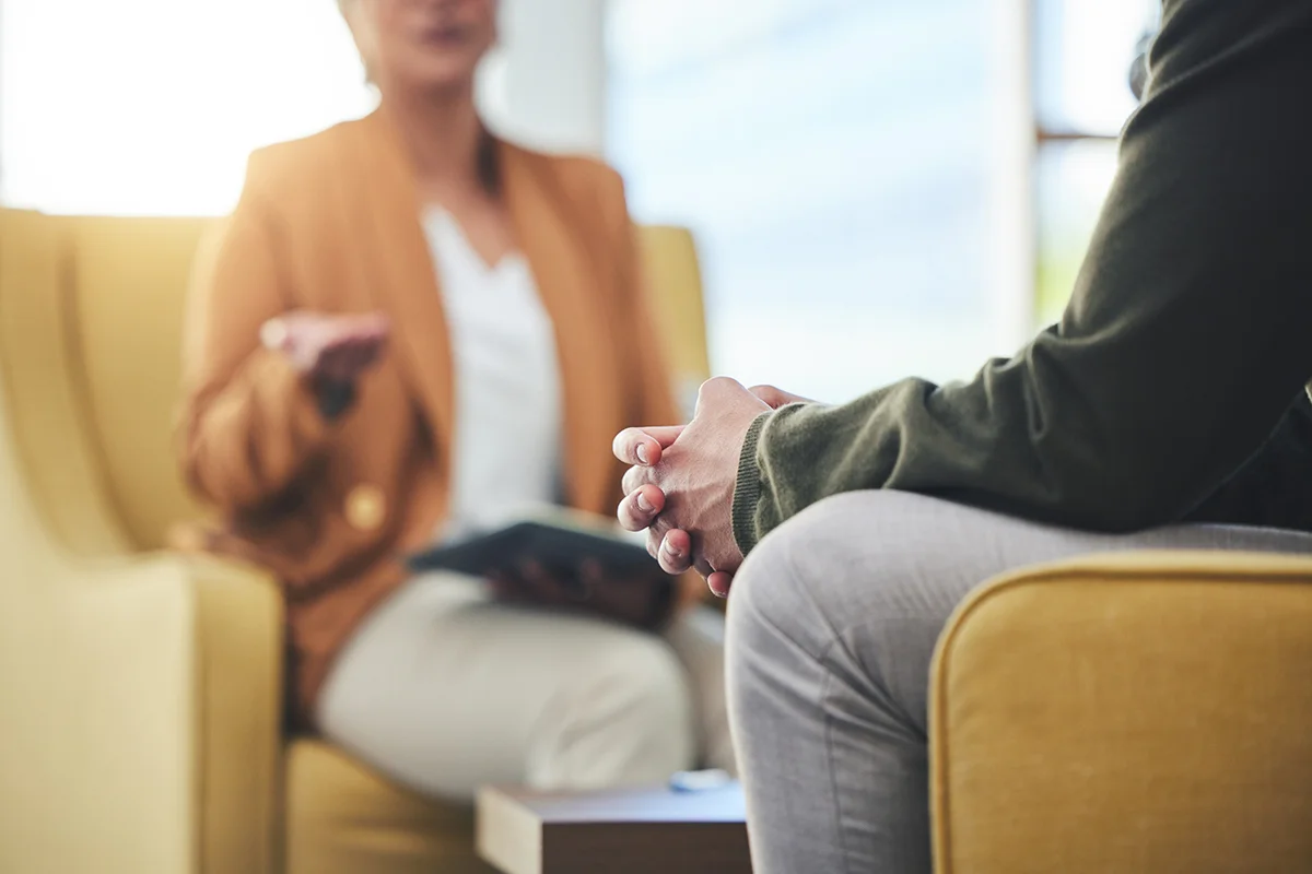 A man sits with hands clasped against his knees while listening to a therapist who sits across from him. He is participating in individual therapy at Olympia Grove Recovery in Ohio.