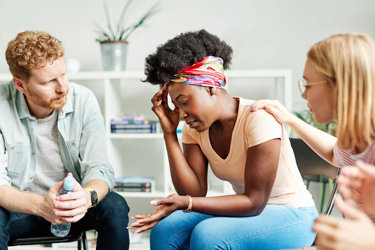 Group therapy session with members supporting woman speaking