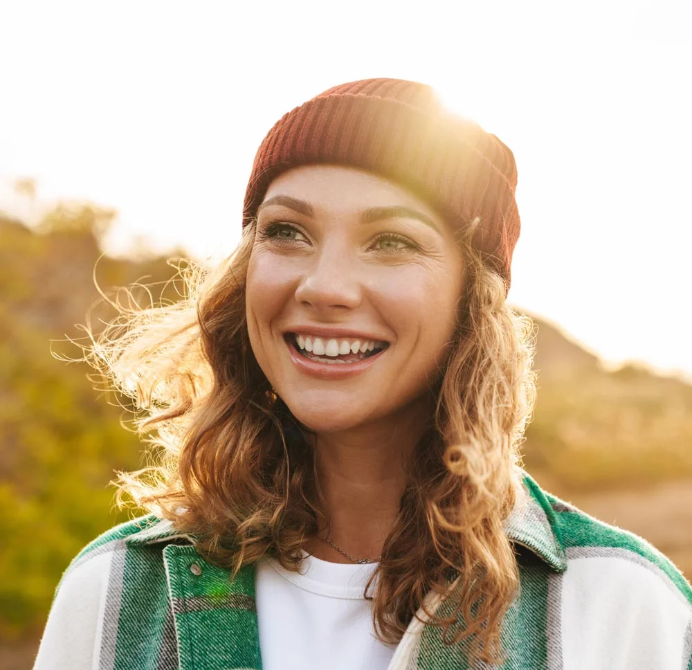 smiling woman with a hat outside during sunset