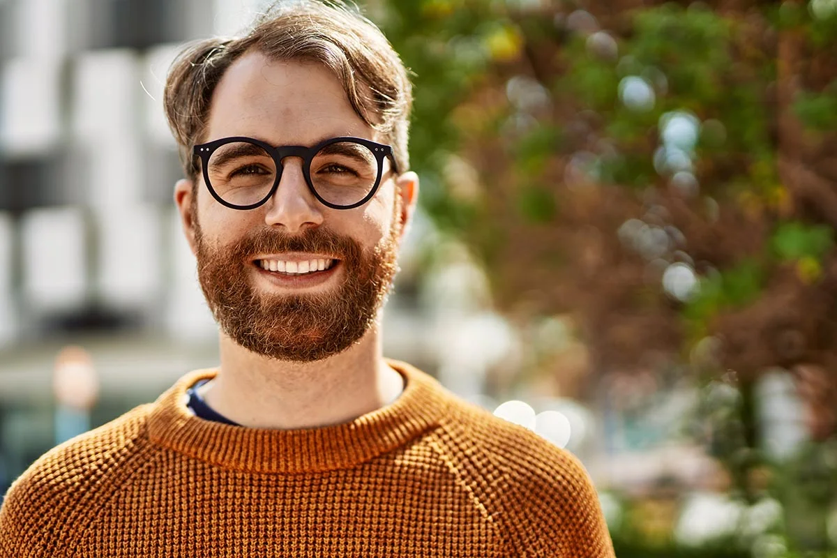smiling man with rounded glasses stands outside ready to enroll in inpatient addiction treatment