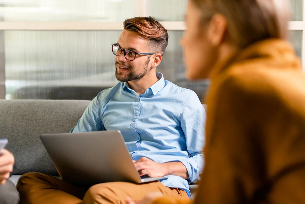 man with a laptop sits on a couch and researches paying for addiction treatment