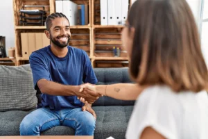man with a beard sits on a couch and shakes hands with his therapist